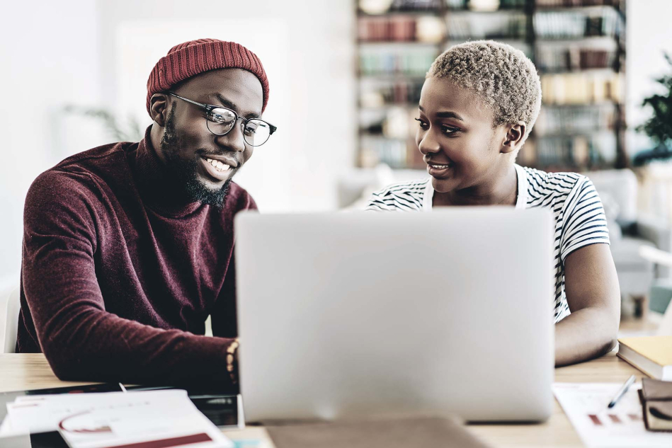 Two people sitting in front of a laptop smiling at each other.