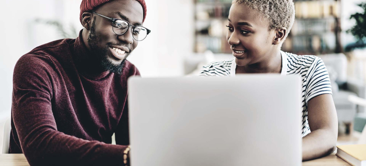 Two people sitting in front of a laptop smiling at each other.